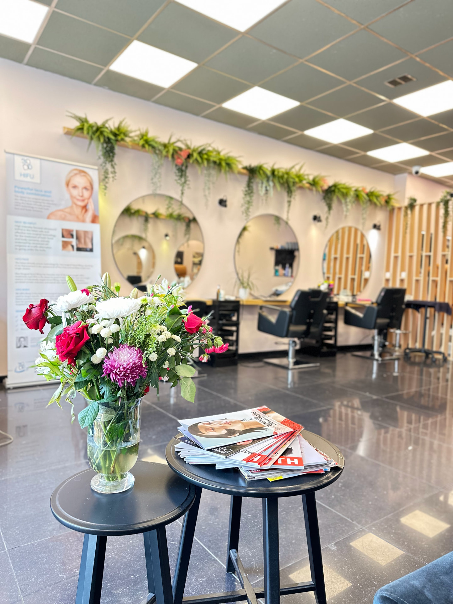 Interior of Chic Salon & Clinic with round styling mirrors, trailing greenery, fresh flowers and salon chairs.