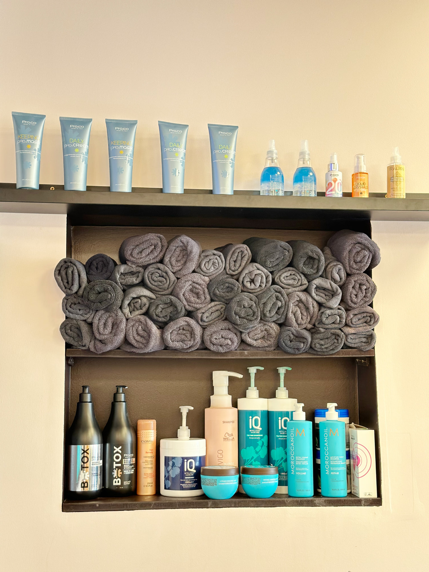 Professional haircare products and rolled towels on the salon shelving.